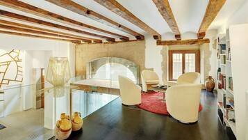 A modern interior with exposed wooden beams, a glass table, white chairs, a red rug, and a bookshelf.