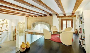 Un interior moderno con vigas de madera a la vista, una mesa de vidrio, sillas blancas, un tapete rojo y una estantería.