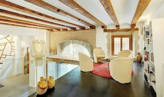 Un interior moderno con vigas de madera a la vista, una mesa de vidrio, sillas blancas, un tapete rojo y una estantería.