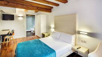 A hotel room with a bed, a desk, a chair, a TV, and a bathroom.