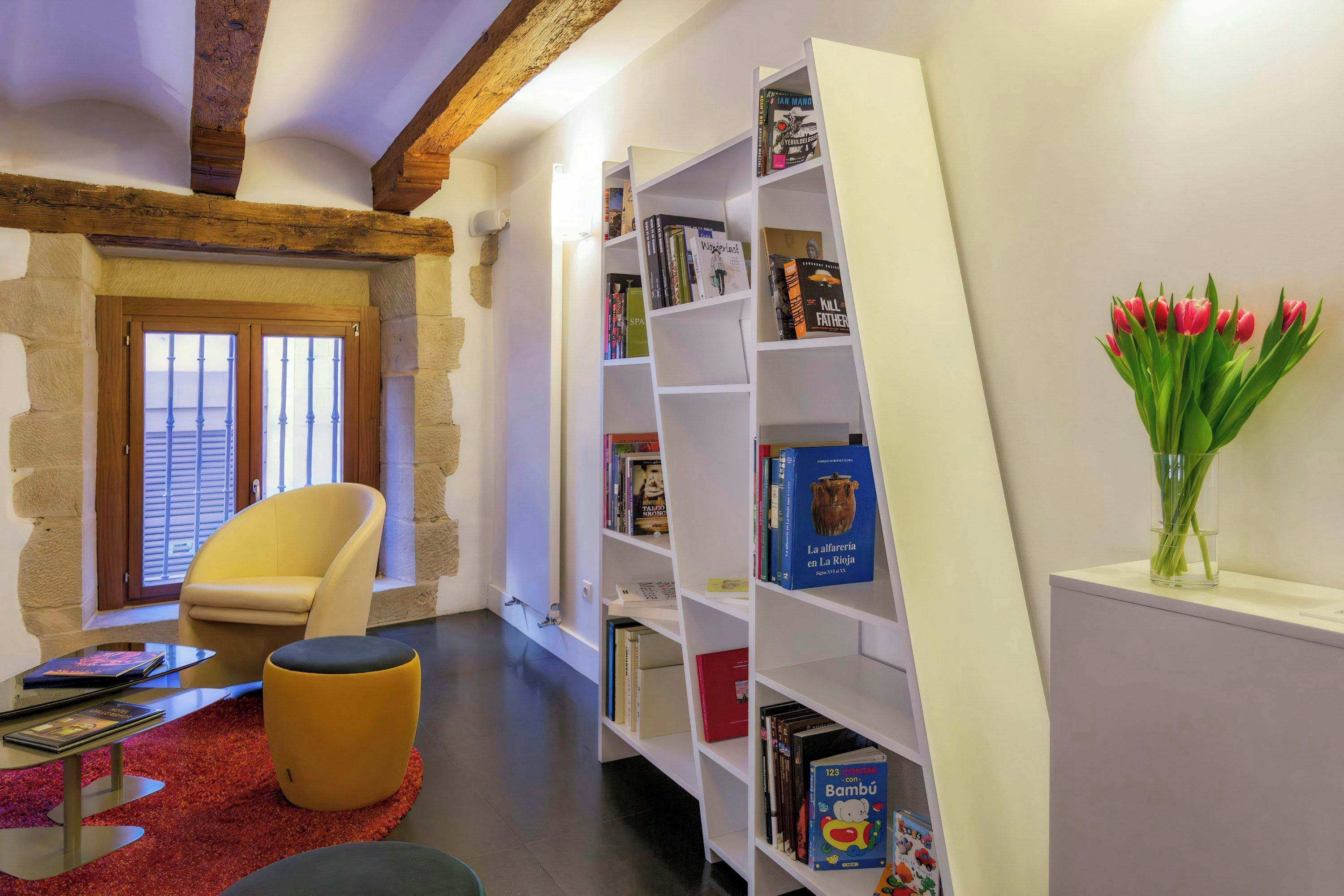 A cozy reading nook with a bookshelf, a chair, and a vase of tulips.