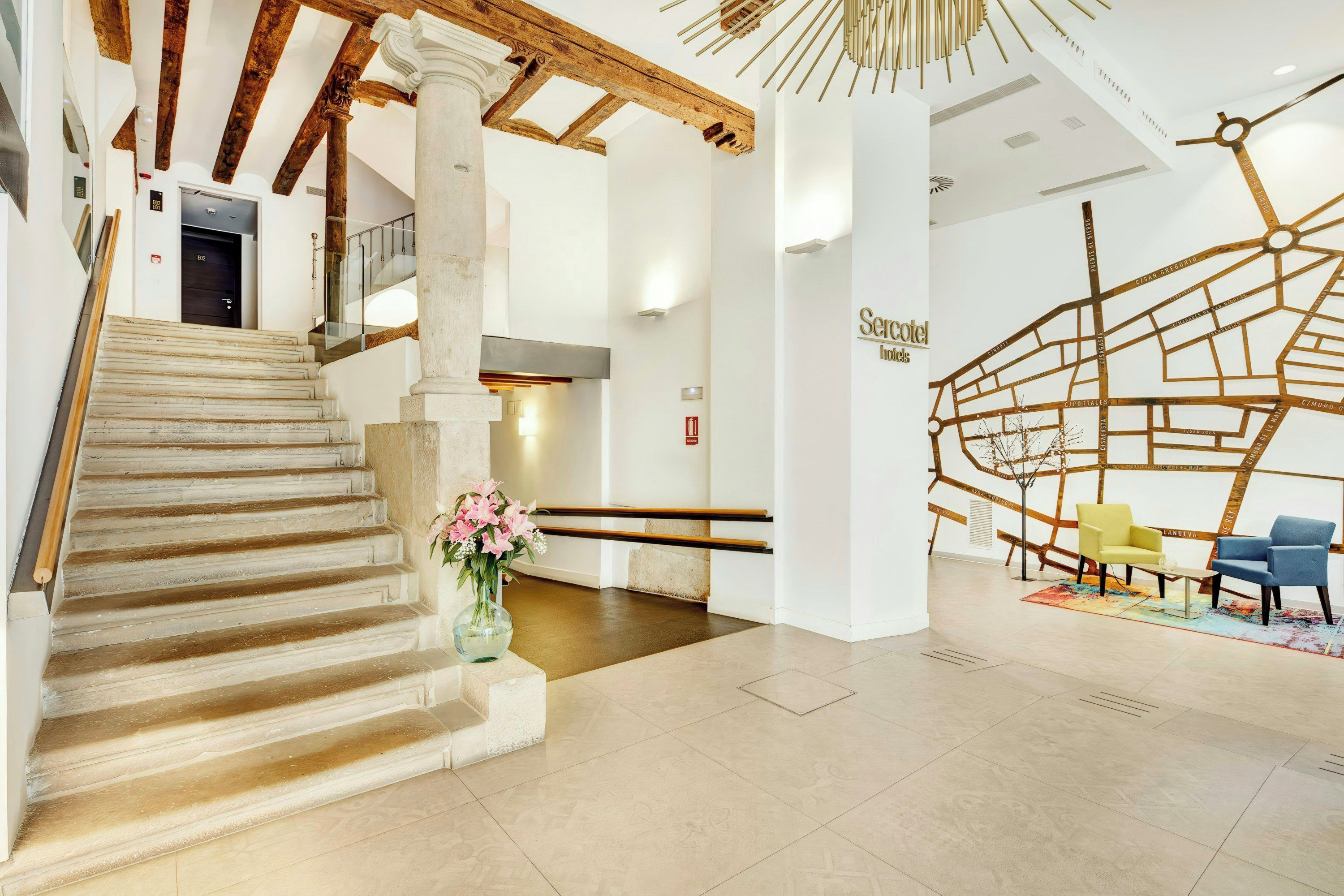A hotel lobby with a staircase, a reception desk, and a seating area with chairs.