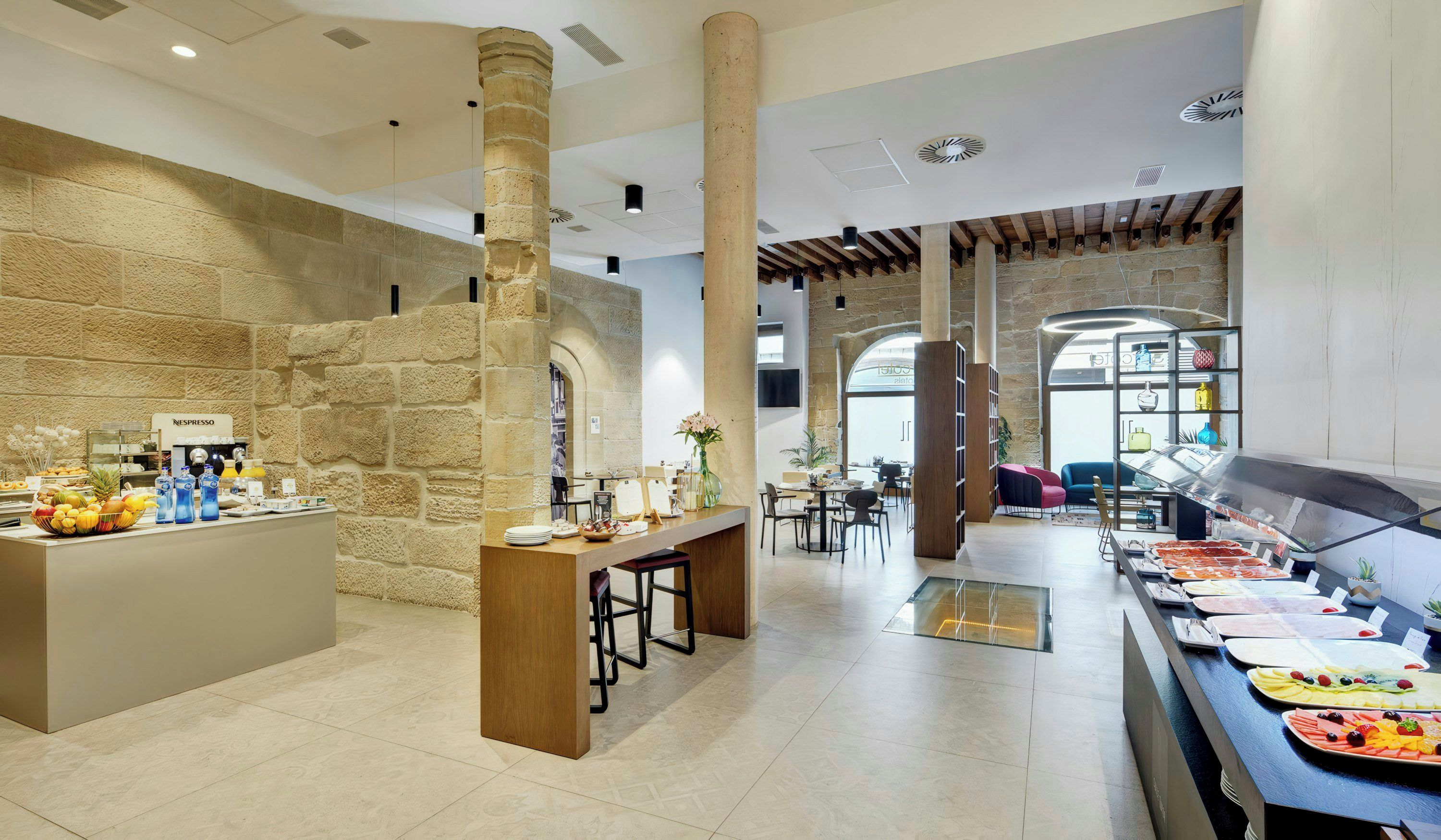 Vestíbulo de hotel con zona de buffet, paredes de piedra y área de descanso con mesas y sillas.
