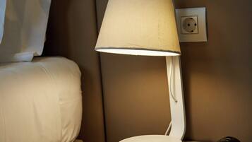 A hotel room with a bedside table, a lamp, a telephone, and a pillow.