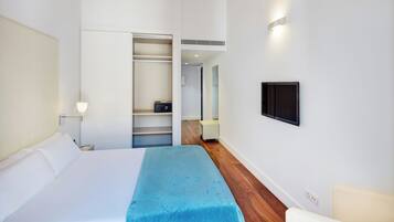 Une chambre d’hôtel comprenant un lit, une table de chevet, une lampe, un téléviseur fixé au mur et un dressing.