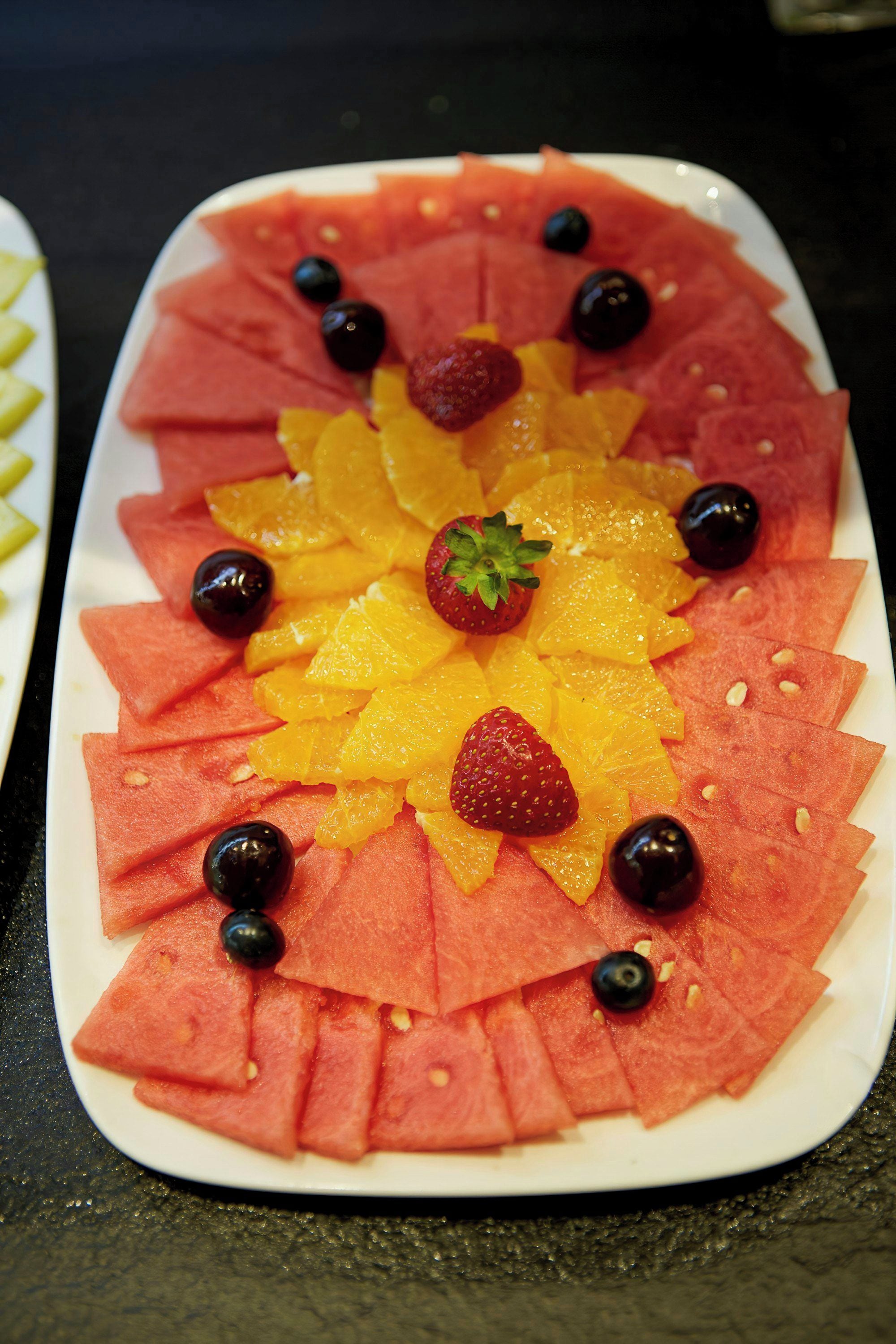A fruit platter with watermelon, orange slices, strawberries, and blueberries arranged on a white plate.