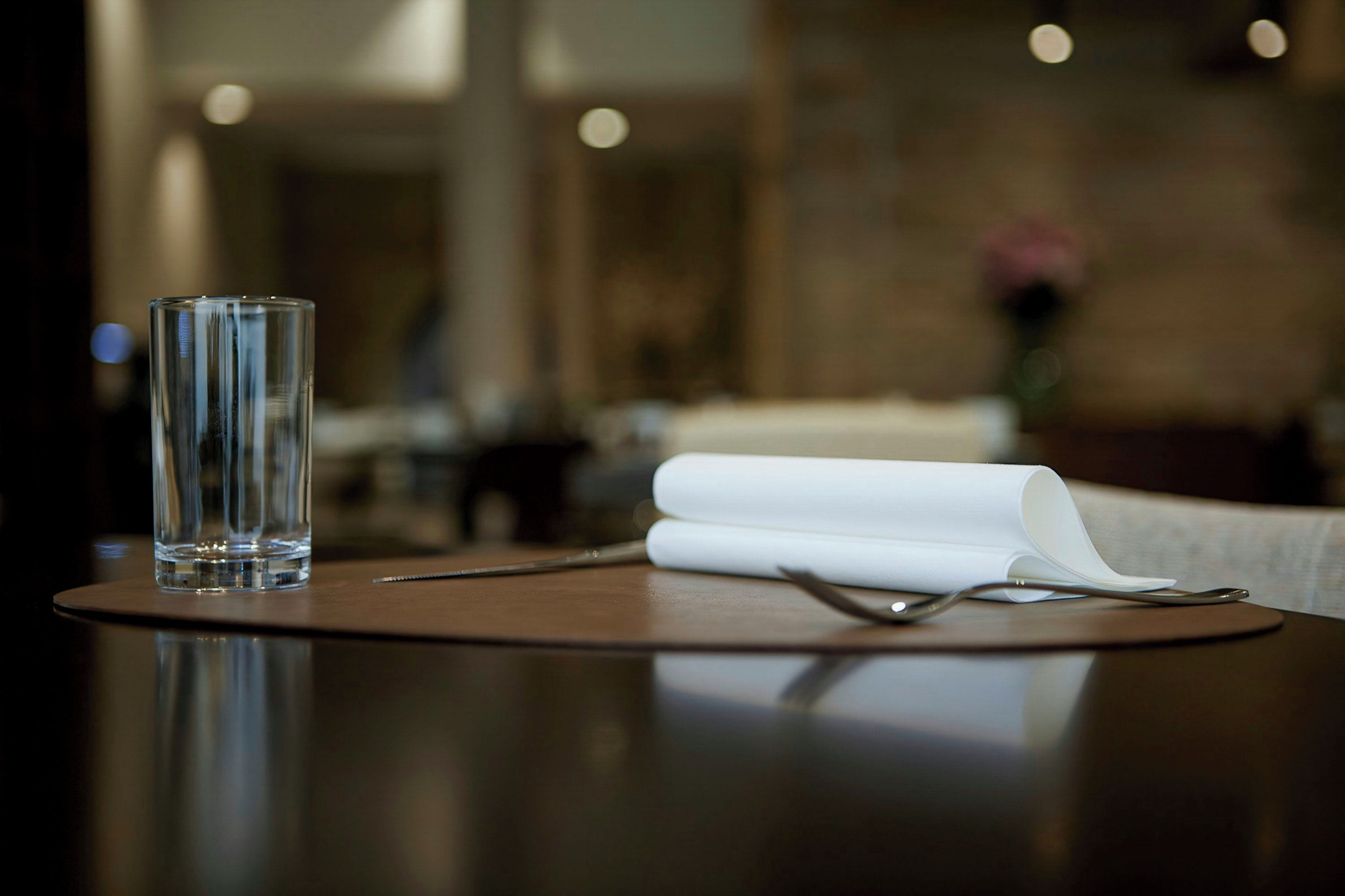 A clear glass on a table with a napkin and cutlery.