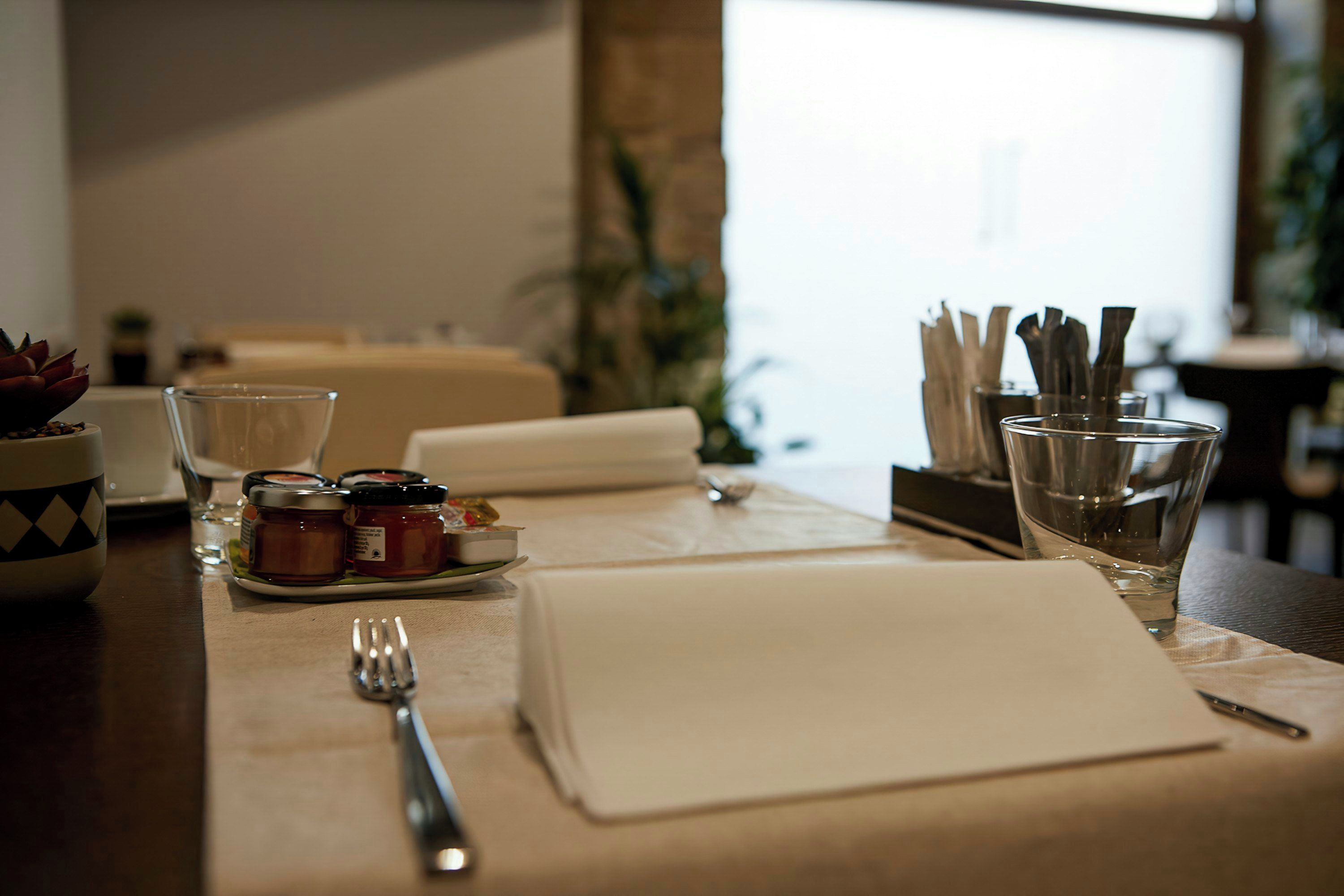 Una mesa de comedor bien dispuesta con un mantel individual blanco, un tenedor, una copa y condimentos.