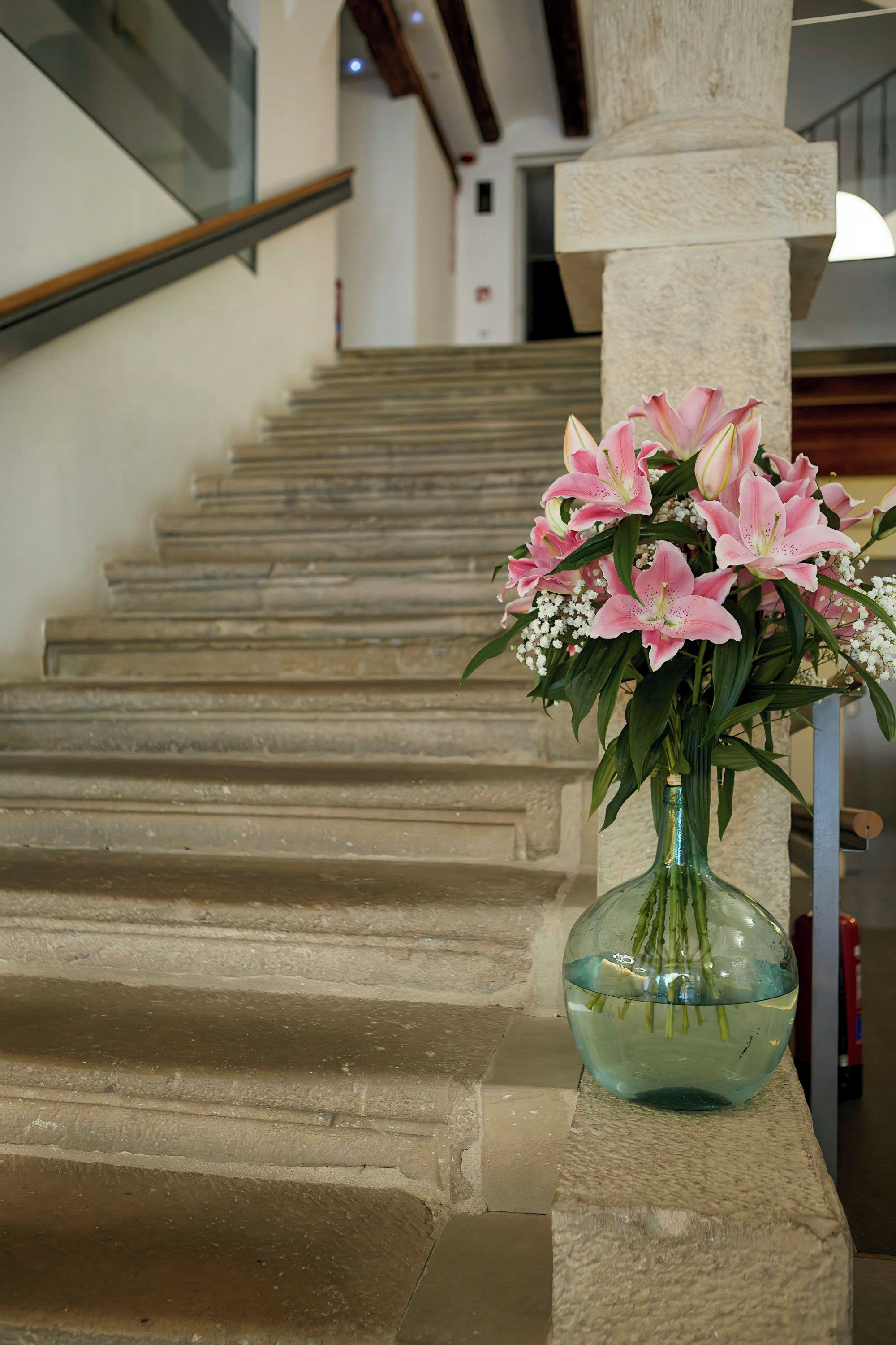 A staircase with a vase of pink lilies on a stone balustrade.