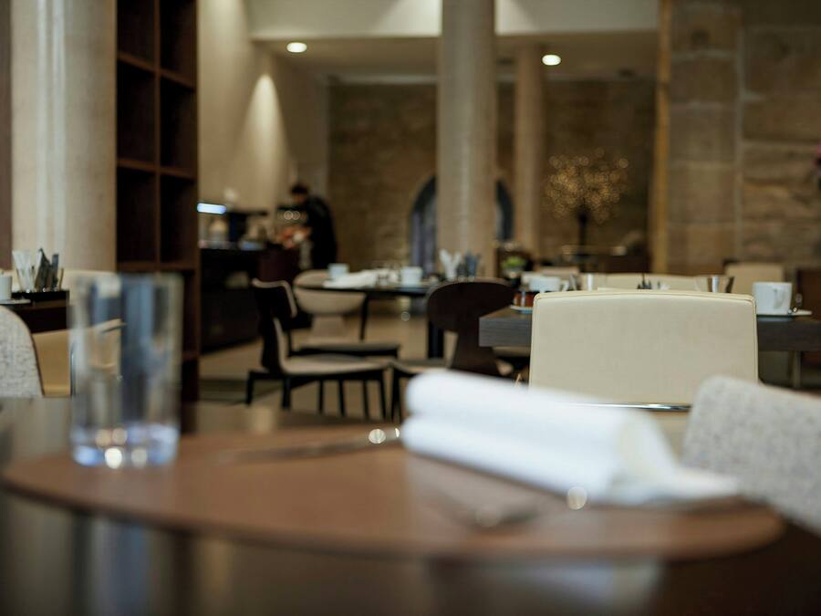 Un comedor con mesas y sillas, una persona al fondo y una pared de piedra.