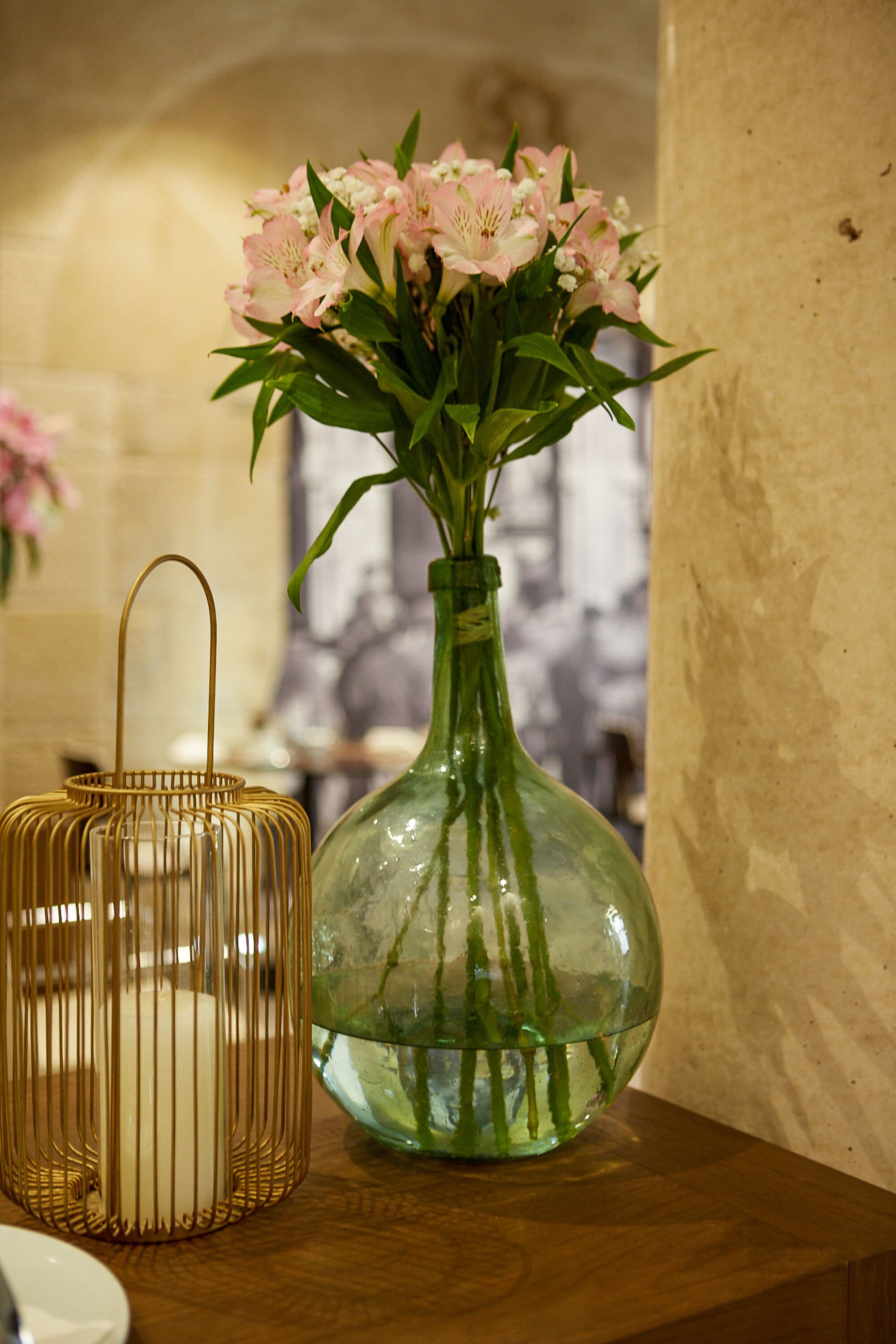 A vase with pink flowers and a candle on a wooden table.