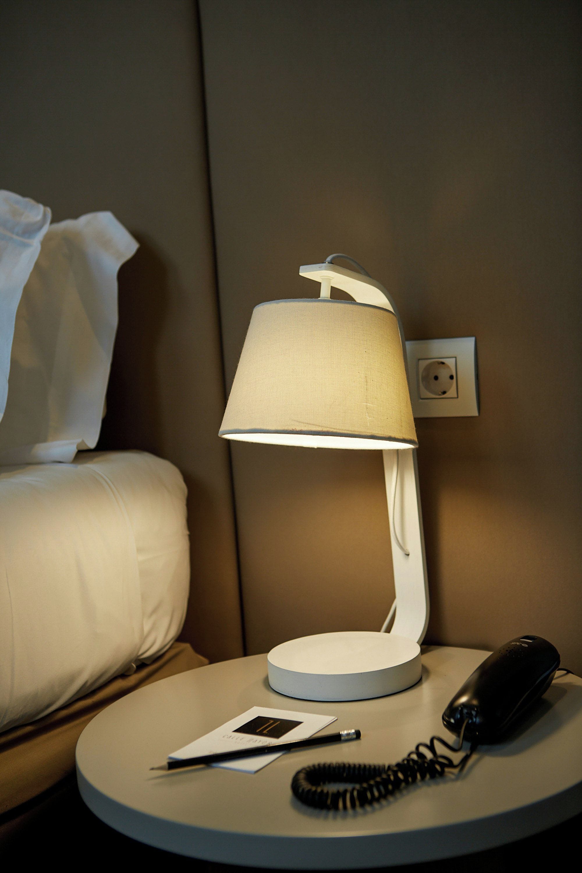 Une chambre d’hôtel avec une table de chevet, une lampe, un téléphone et un oreiller.
