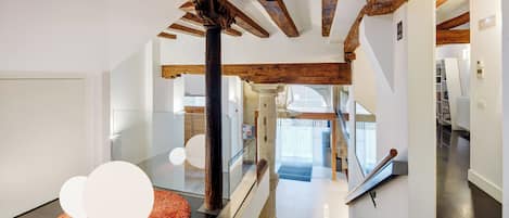 A modern interior with exposed wooden beams, a glass railing, and a staircase leading to a second floor.