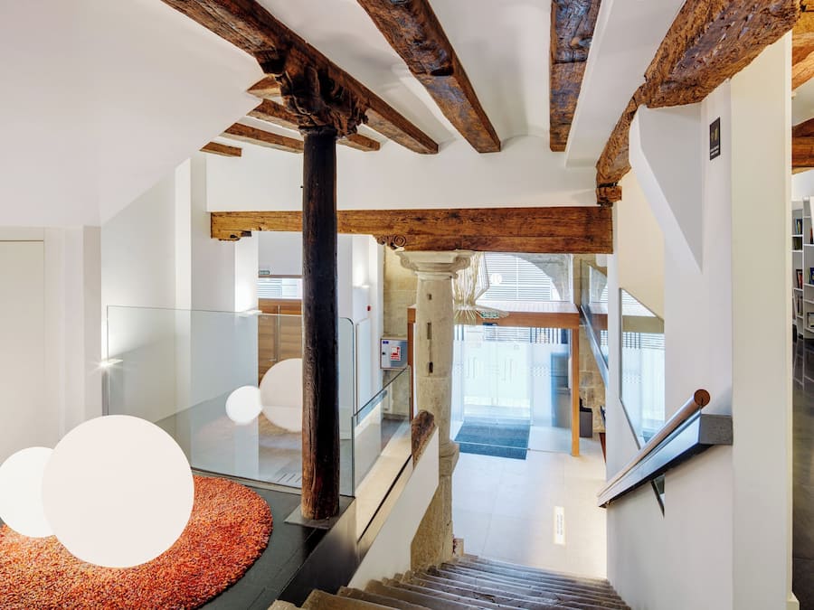A modern interior with exposed wooden beams, a glass railing, and a staircase leading to a second floor.