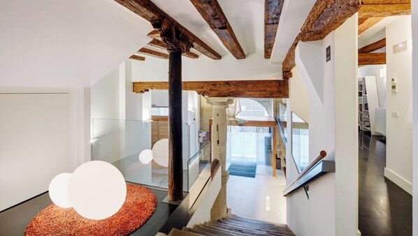 A modern interior with exposed wooden beams, a glass railing, and a staircase leading to a second floor.