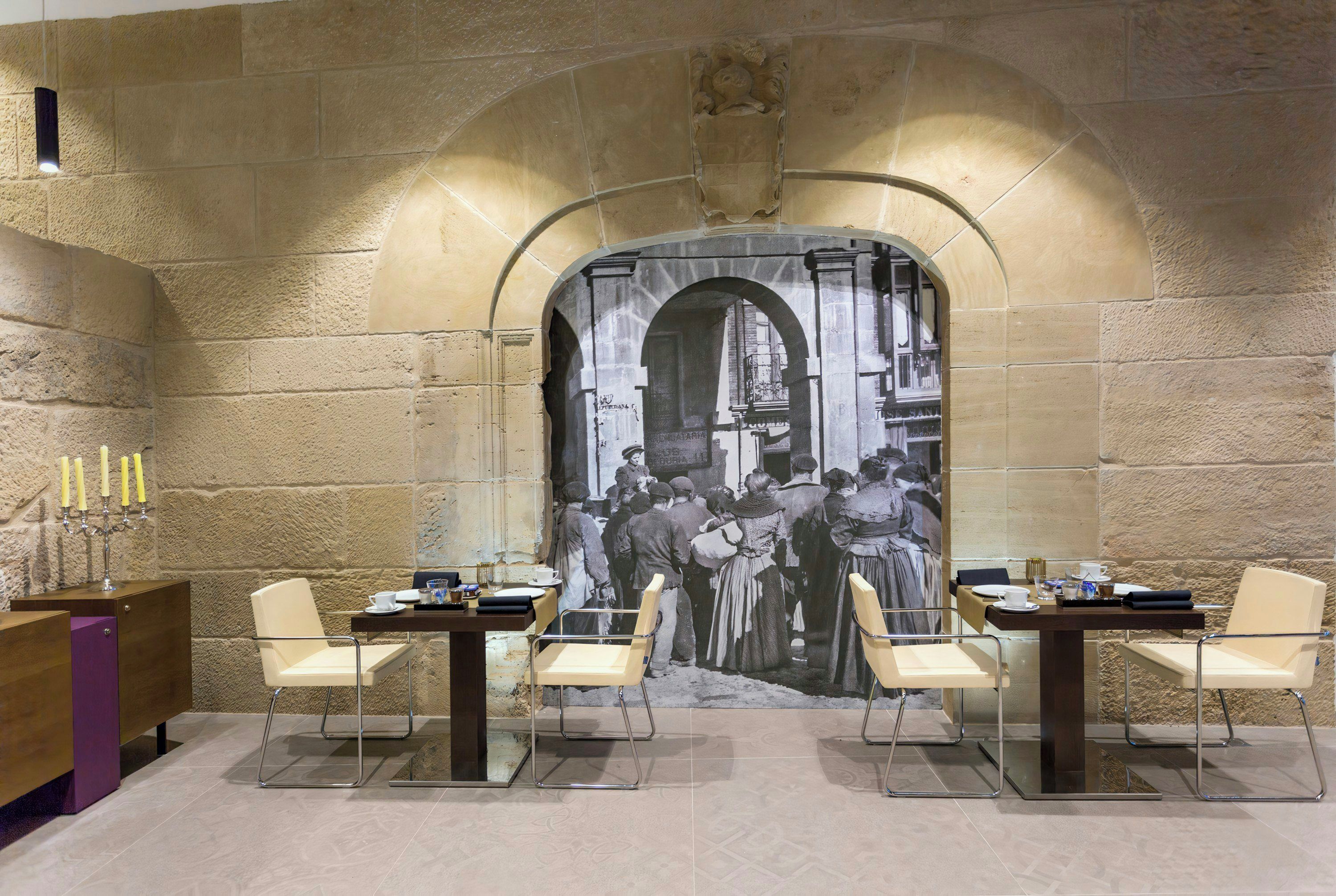 Un comedor con un mural, mesas, sillas y un candelabro.