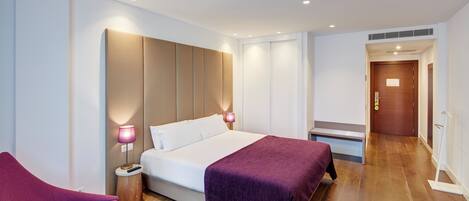 Una habitación de hotel moderna con una cama grande, dos lámparas de noche, suelo de madera y una puerta de madera.