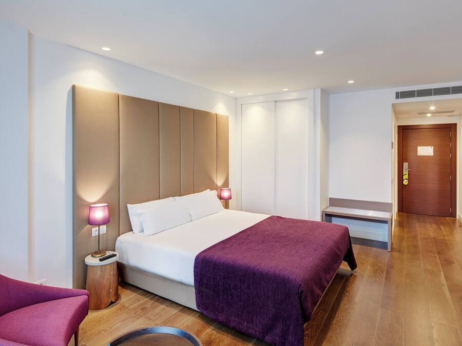 Una habitación de hotel moderna con una cama grande, dos lámparas de noche, suelo de madera y una puerta de madera.
