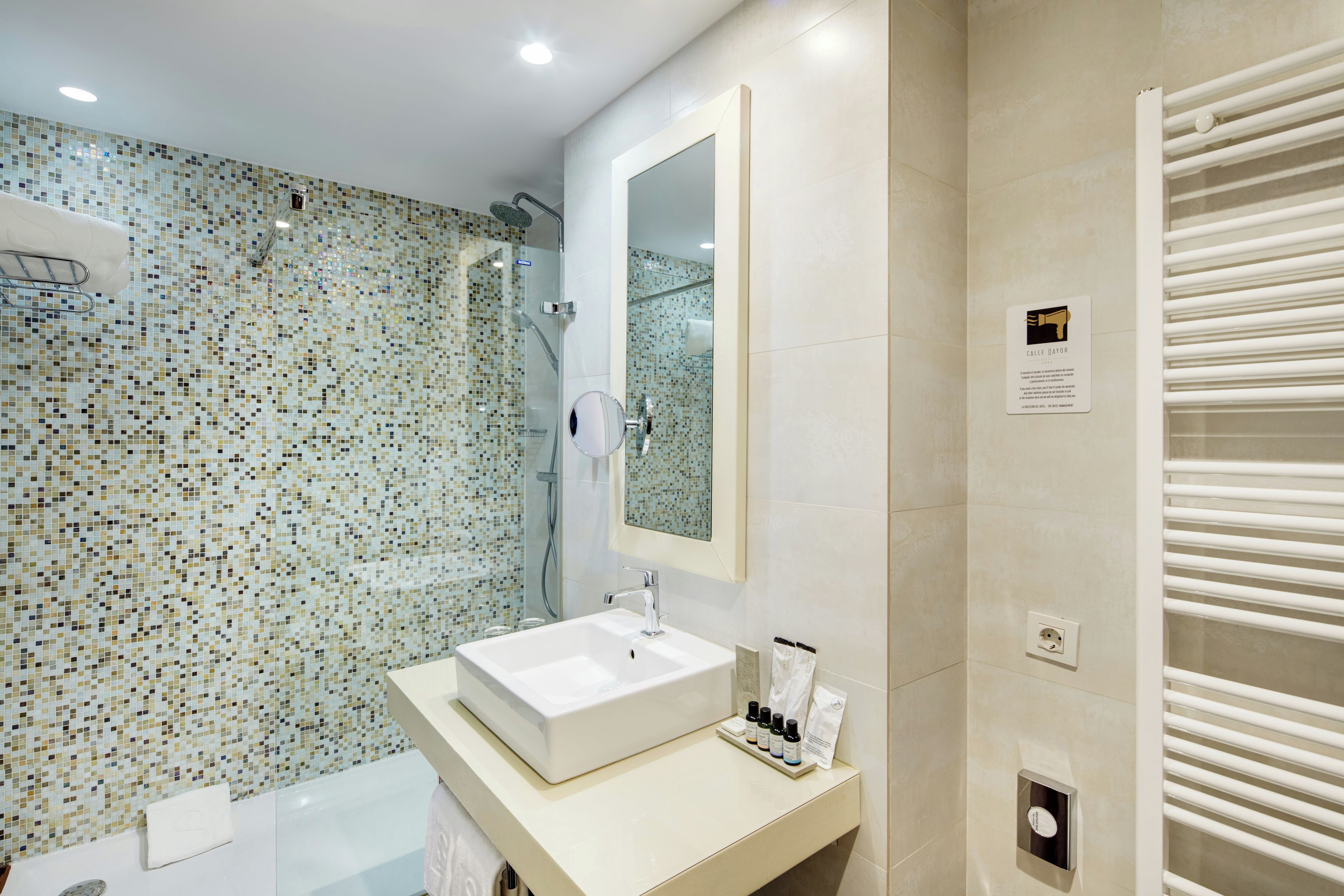 A modern bathroom with a glass-enclosed shower, a large mirror, and a white sink with toiletries.