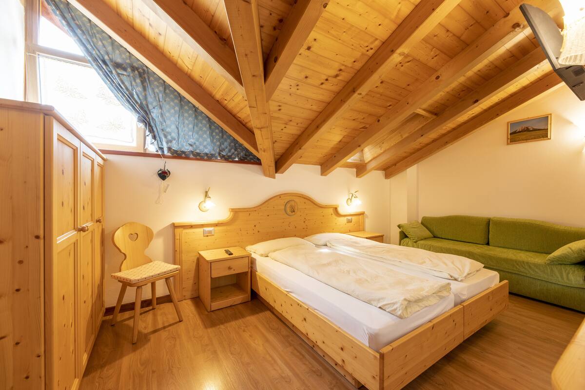 A wooden bedroom with a bed, a green sofa, a wooden wardrobe, and a small table.