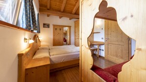 A wooden room with a bed, a red carpet, and a wooden door. - Affittacamere Corradini (Castello-Molina di Fiemme)