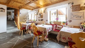 A dining area with wooden tables and chairs, stone flooring, and a staircase leading to another level. - Affittacamere Corradini (Castello-Molina di Fiemme)