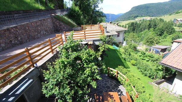 A stone retaining wall, wooden deck, and a view of a rural landscape with houses and greenery. - Affittacamere Corradini (Castello-Molina di Fiemme)