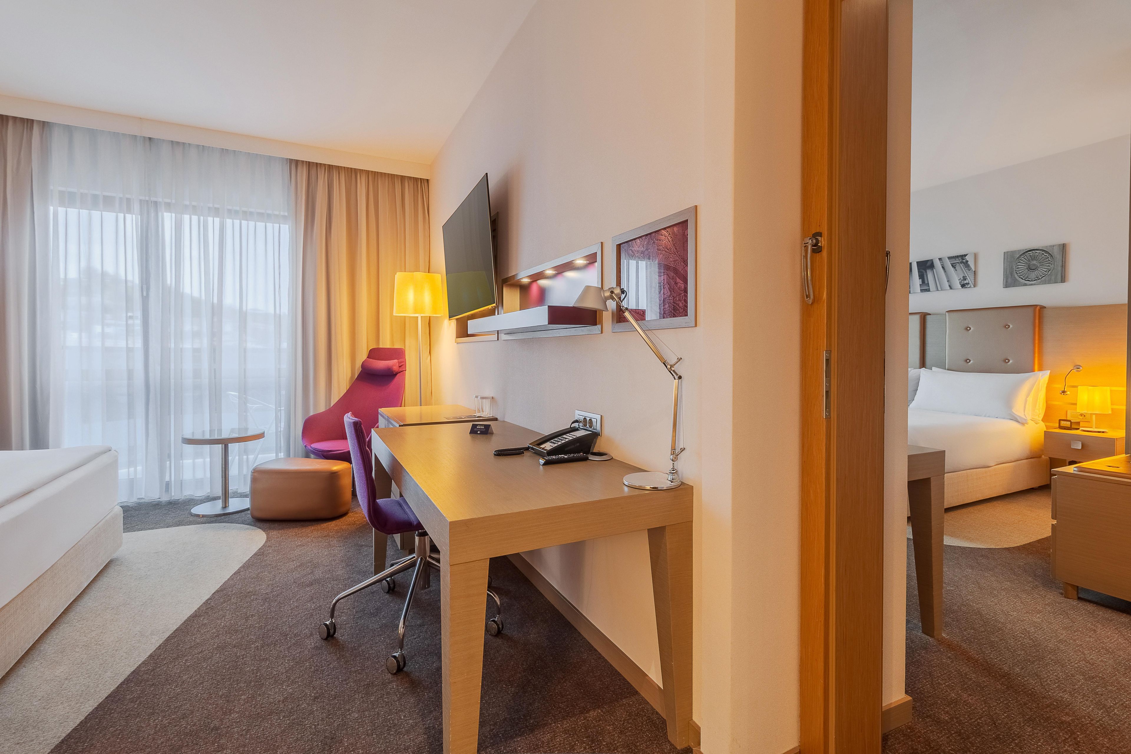 Een hotelkamer met een bed, een bureau, een stoel, een televisie en een nachtkastje met een lamp.
