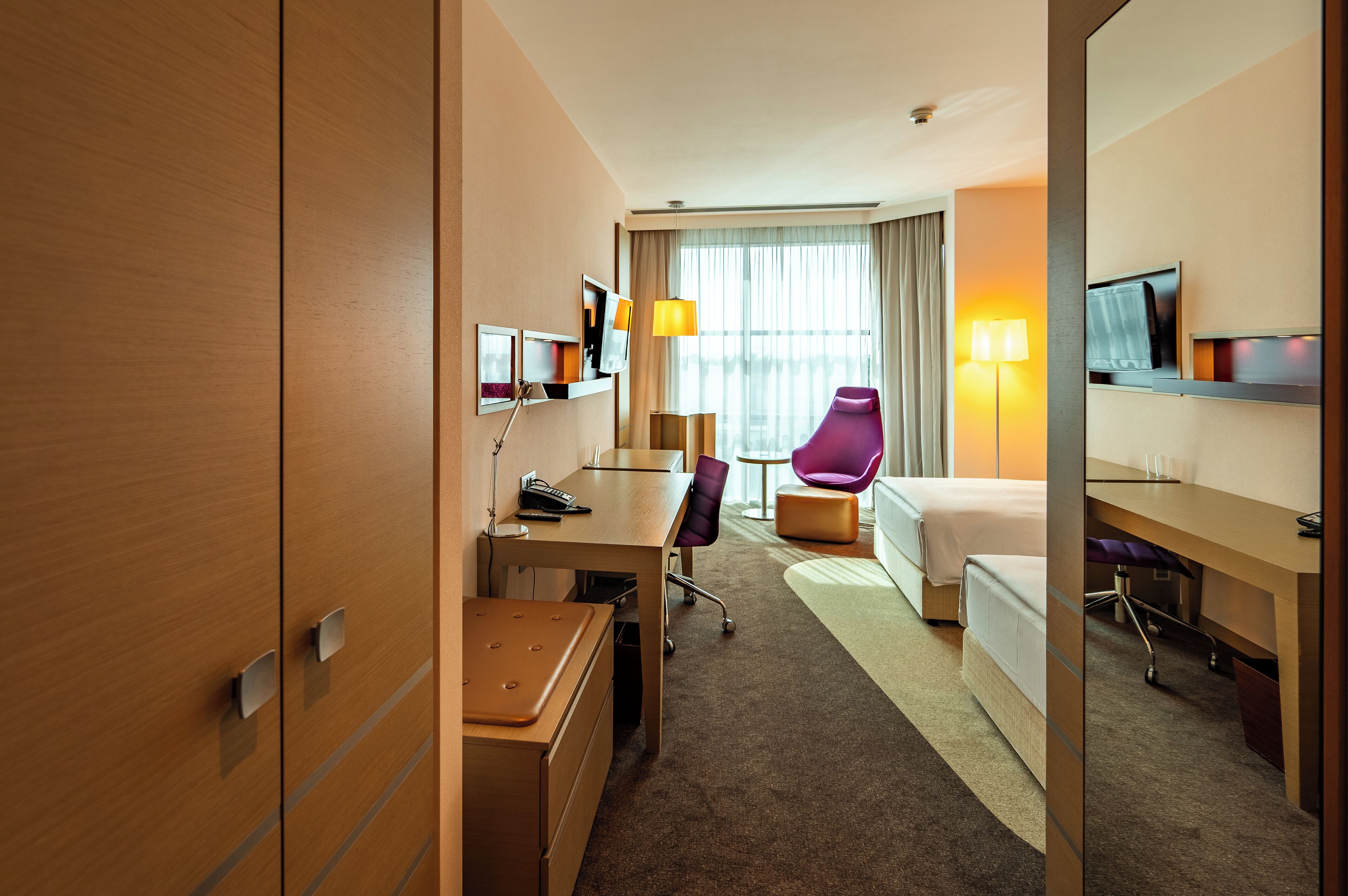 A hotel room with a bed, desk, chair, and a television.