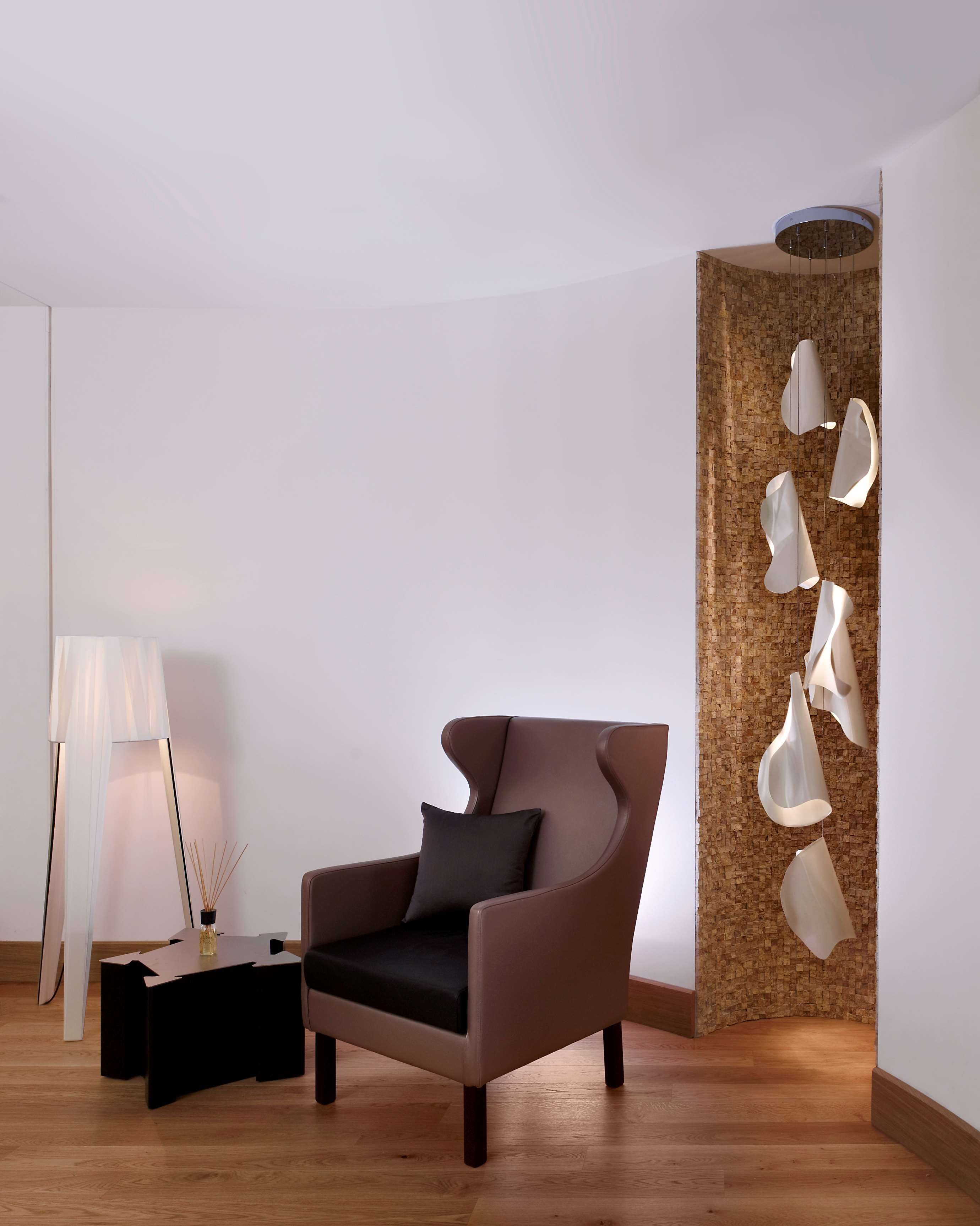 Una habitación moderna con un sillón marrón, una mesita auxiliar, una lámpara y un elemento decorativo único con luces colgantes.