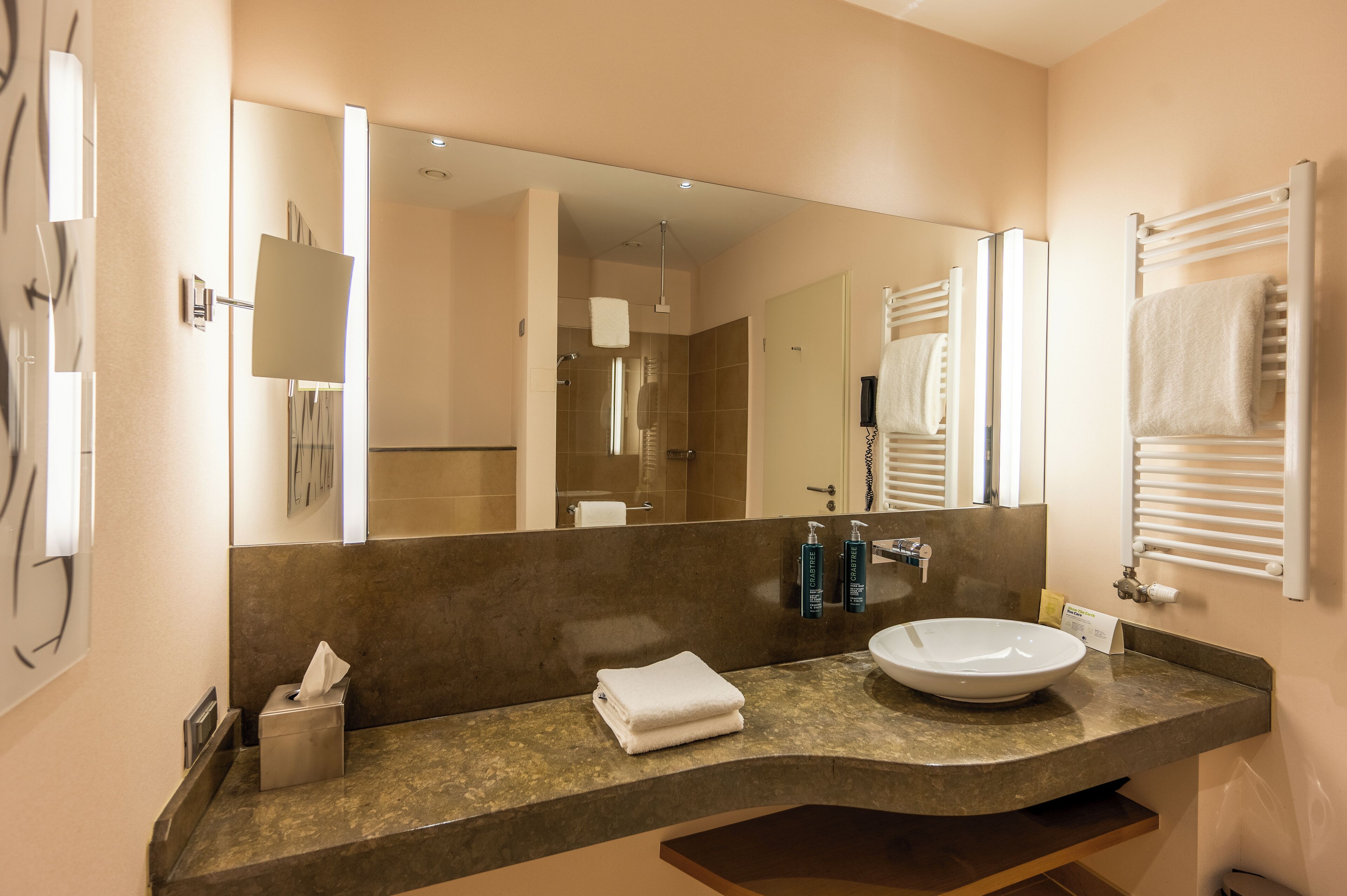A modern bathroom with a large mirror, a sink, and a towel rack.