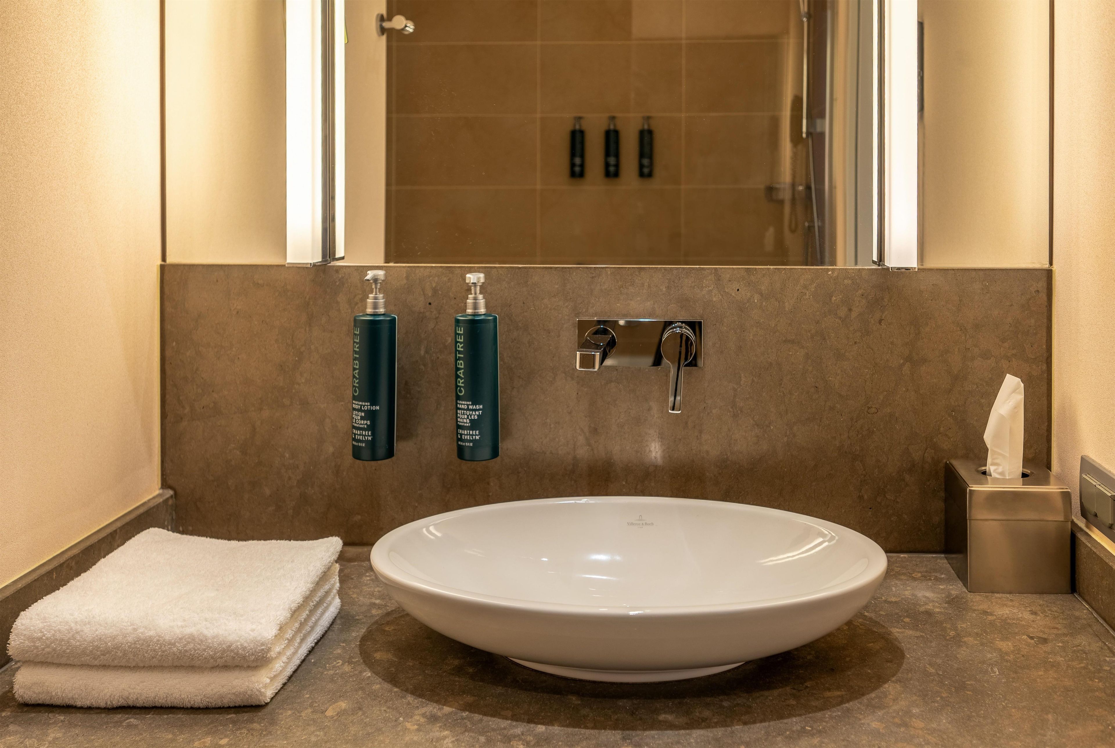A bathroom with a large white sink, a towel, and two hand wash bottles.