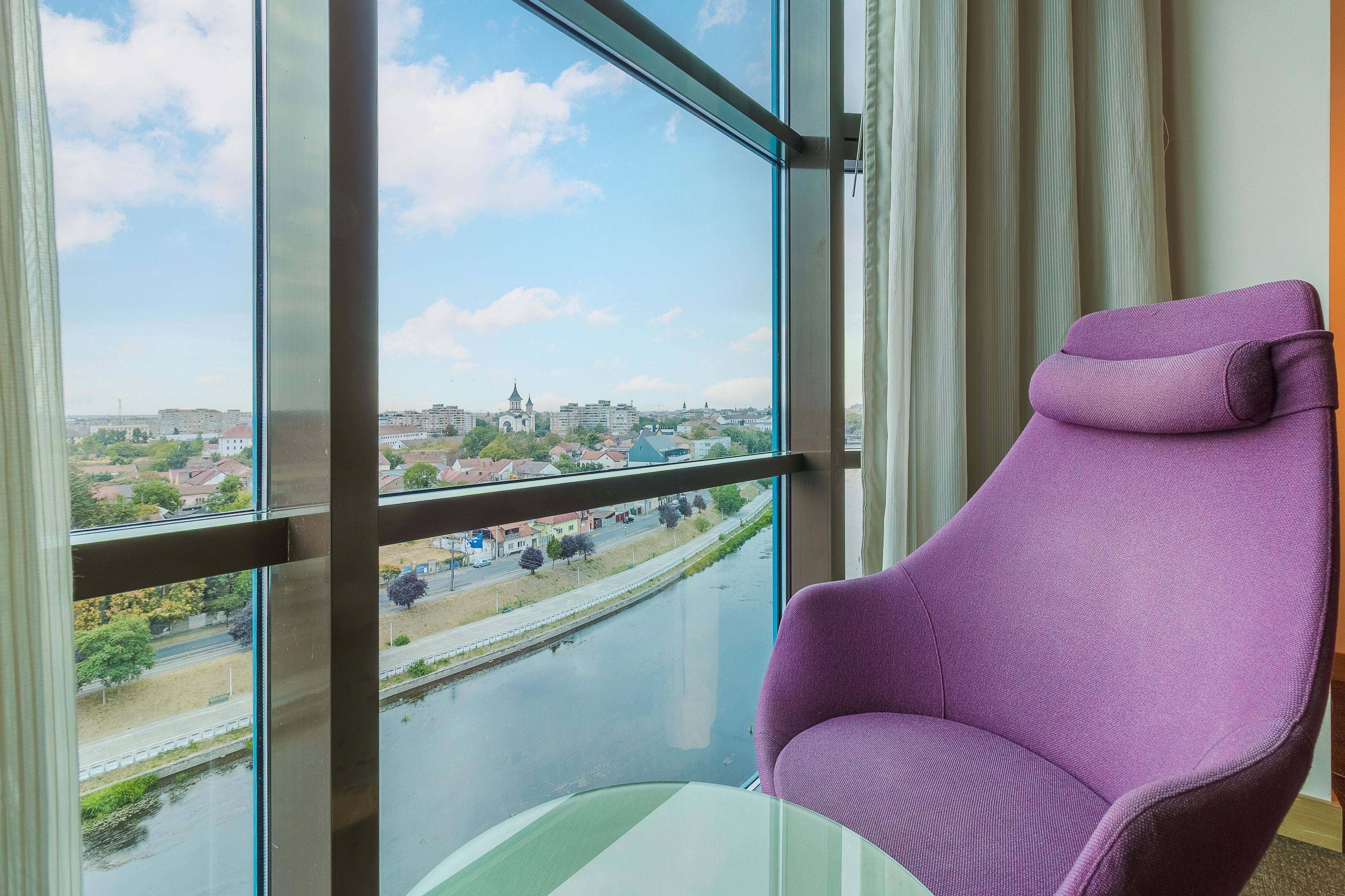 A room with a large window, a purple chair, and a view of a cityscape.