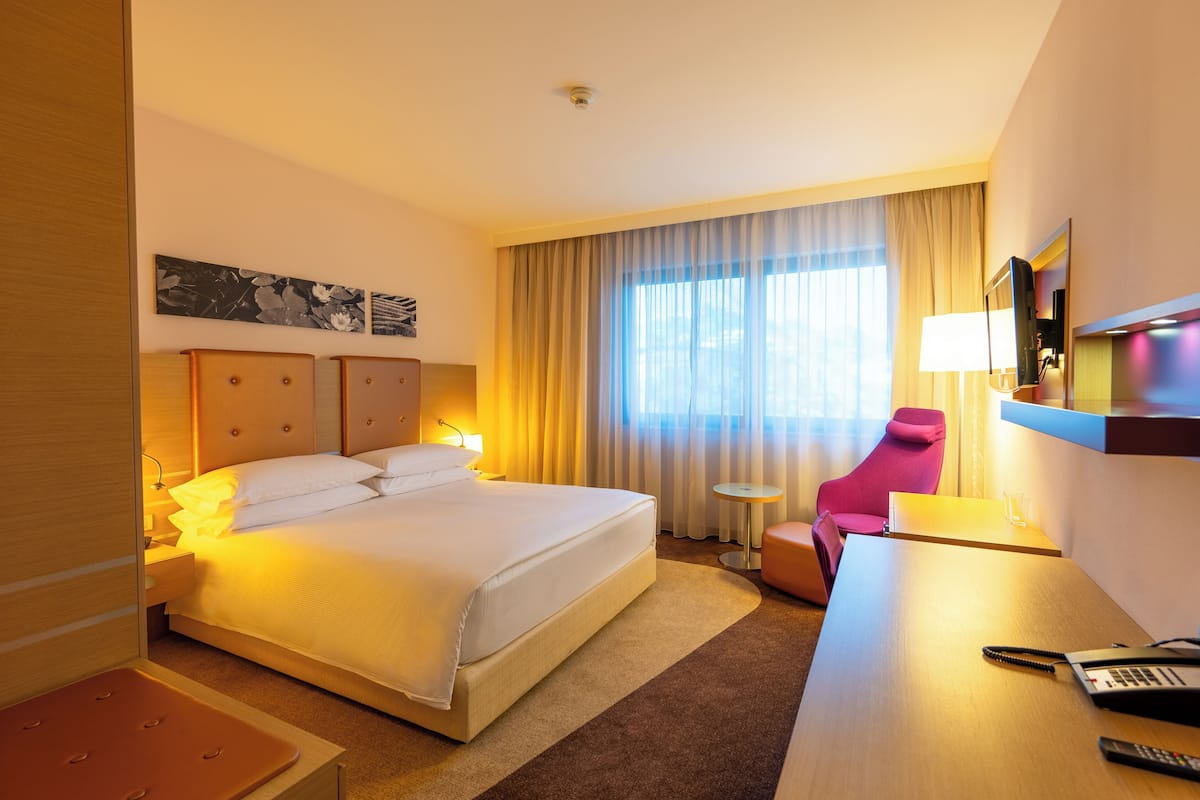 Una habitación de hotel con una cama grande, un escritorio con lámpara, una silla y un televisor.