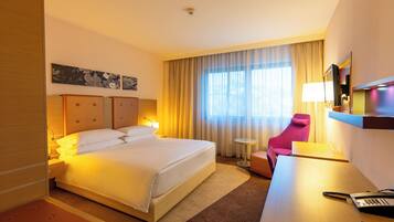 A hotel room with a large bed, a desk with a lamp, a chair, and a television.