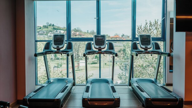 Three treadmills aligned in front of large windows with a view of a residential area. - DoubleTree by Hilton Hotel Oradea (Oradea)