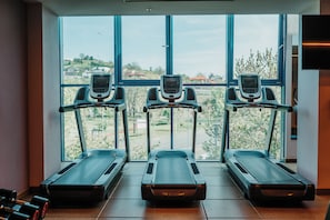 Three treadmills aligned in front of large windows with a view of a residential area. - DoubleTree by Hilton Hotel Oradea (Oradea)