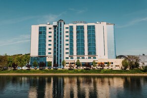 Un hotel grande y moderno con varios pisos y una torre cilíndrica central, ubicado junto a una masa de agua.