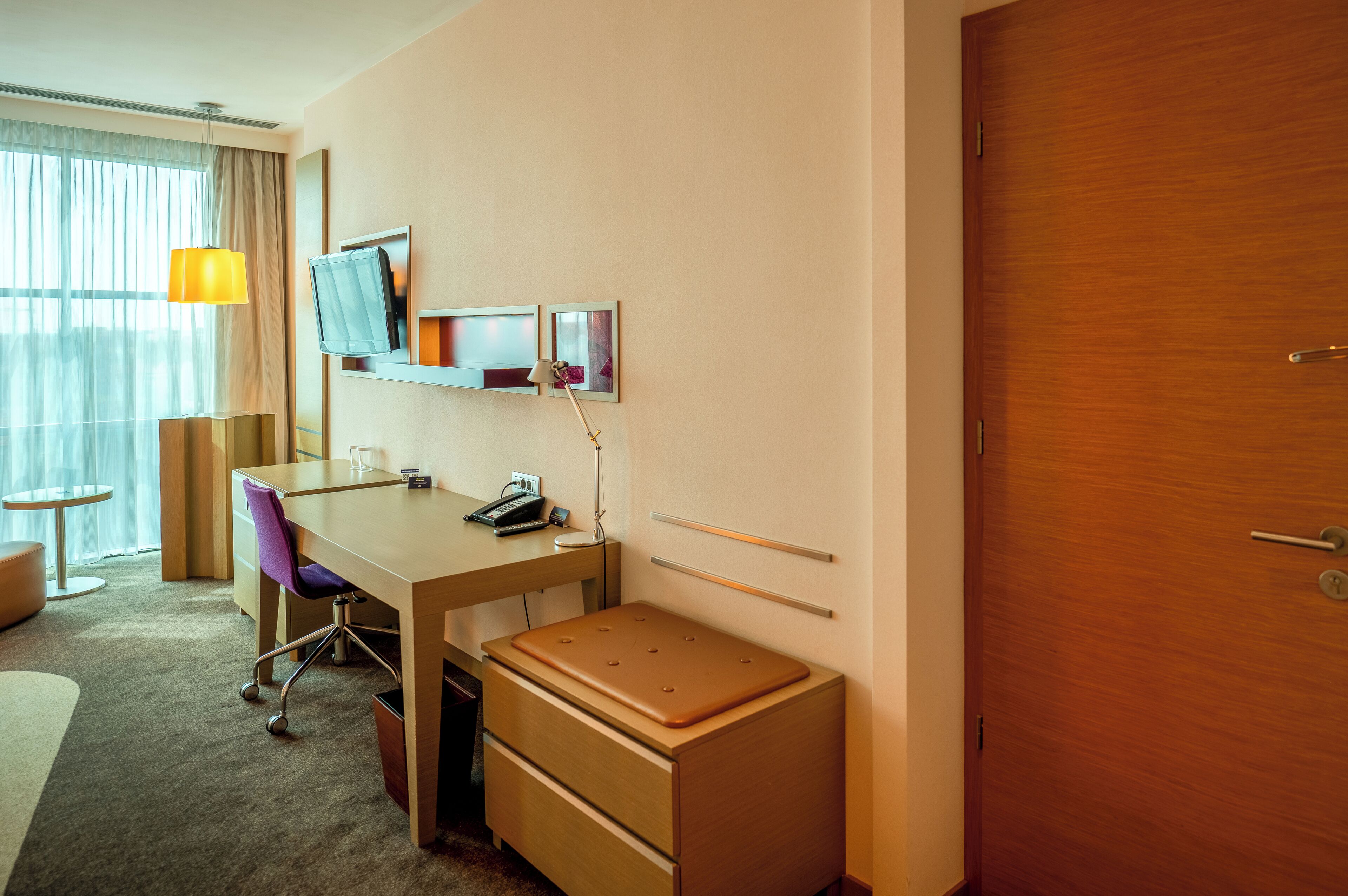 Habitación de hotel con un escritorio de madera, una silla, una mesita, una lámpara, un espejo y un armario.