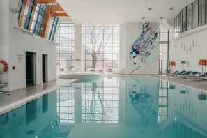 A large indoor swimming pool with clear glass walls, a mural on the wall, and lounge chairs along the side. - DoubleTree by Hilton Hotel Oradea (Oradea)