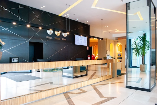 A modern hotel reception area with a digital screen, a clock, and a sign indicating the hotel's location in London and New York. - DoubleTree by Hilton Hotel Oradea (Oradea)