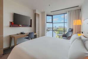 Une chambre d’hôtel avec un grand lit, un bureau, une chaise, un téléviseur fixé au mur et une fenêtre donnant sur la ville.
