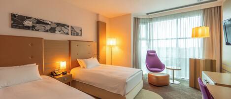 A hotel room with two beds, a desk, a chair, a TV, and a window with curtains.