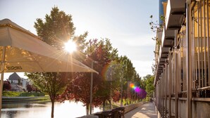 An outdoor café with tables and chairs, a river in the background, and a building with a row of windows on the right. - DoubleTree by Hilton Hotel Oradea (Oradea)