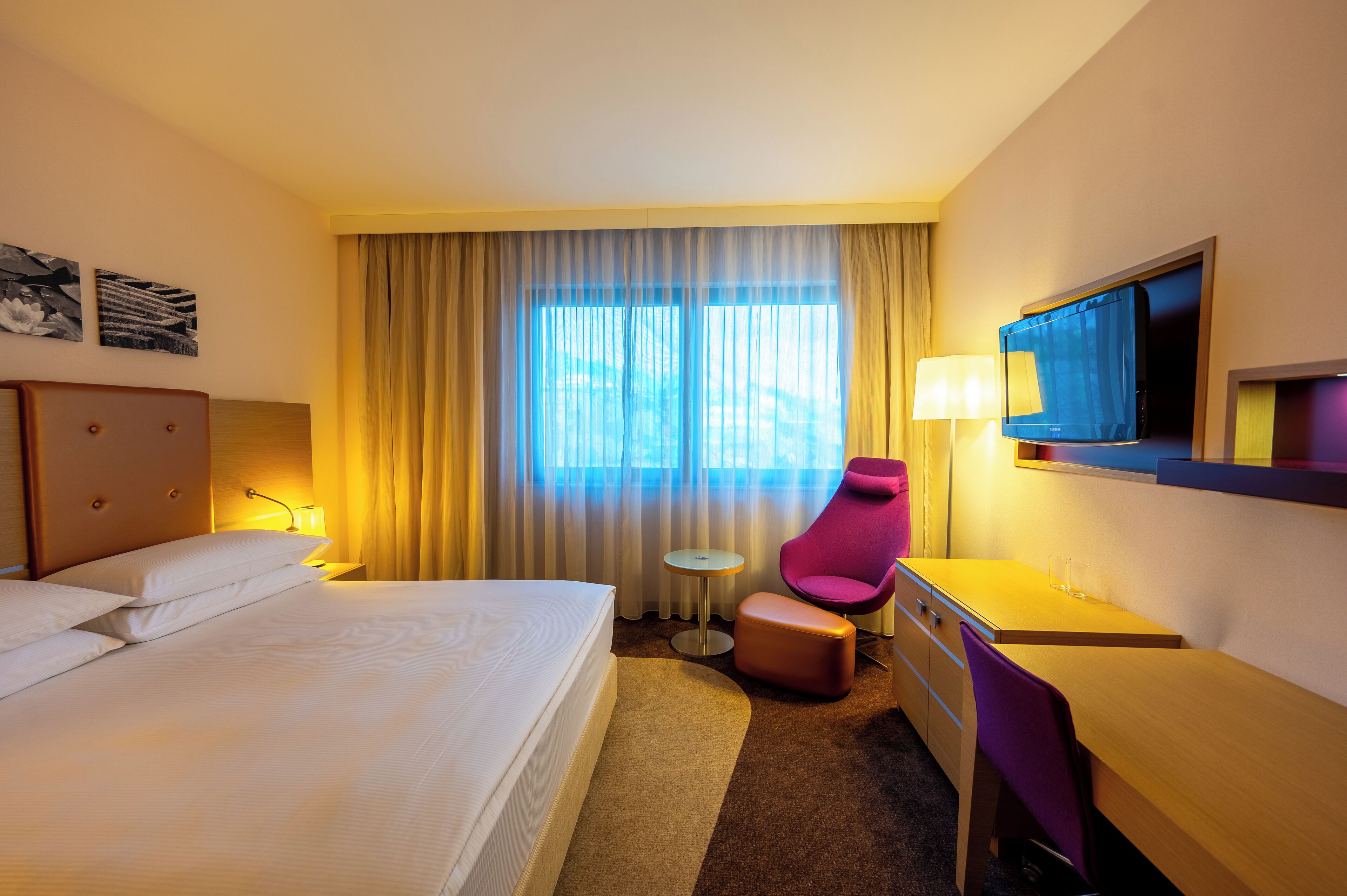 Habitación de hotel con una cama grande, un escritorio, una silla, un televisor y una ventana con cortinas.