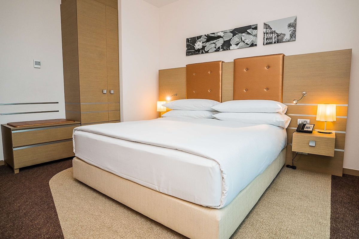 Une chambre d’hôtel avec un lit, des tables de chevet, une armoire et des œuvres d’art accrochées au mur.