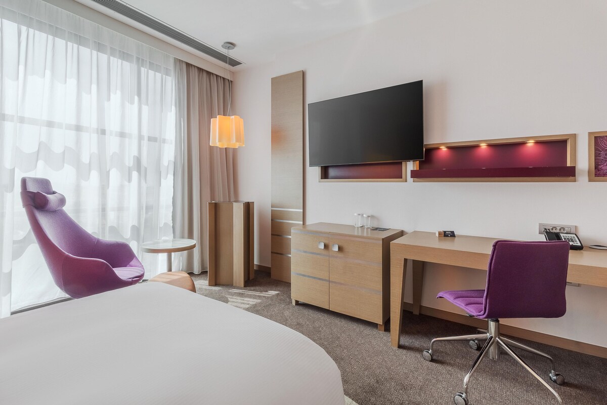 A hotel room with a bed, a desk, a chair, a television, and a window with curtains.