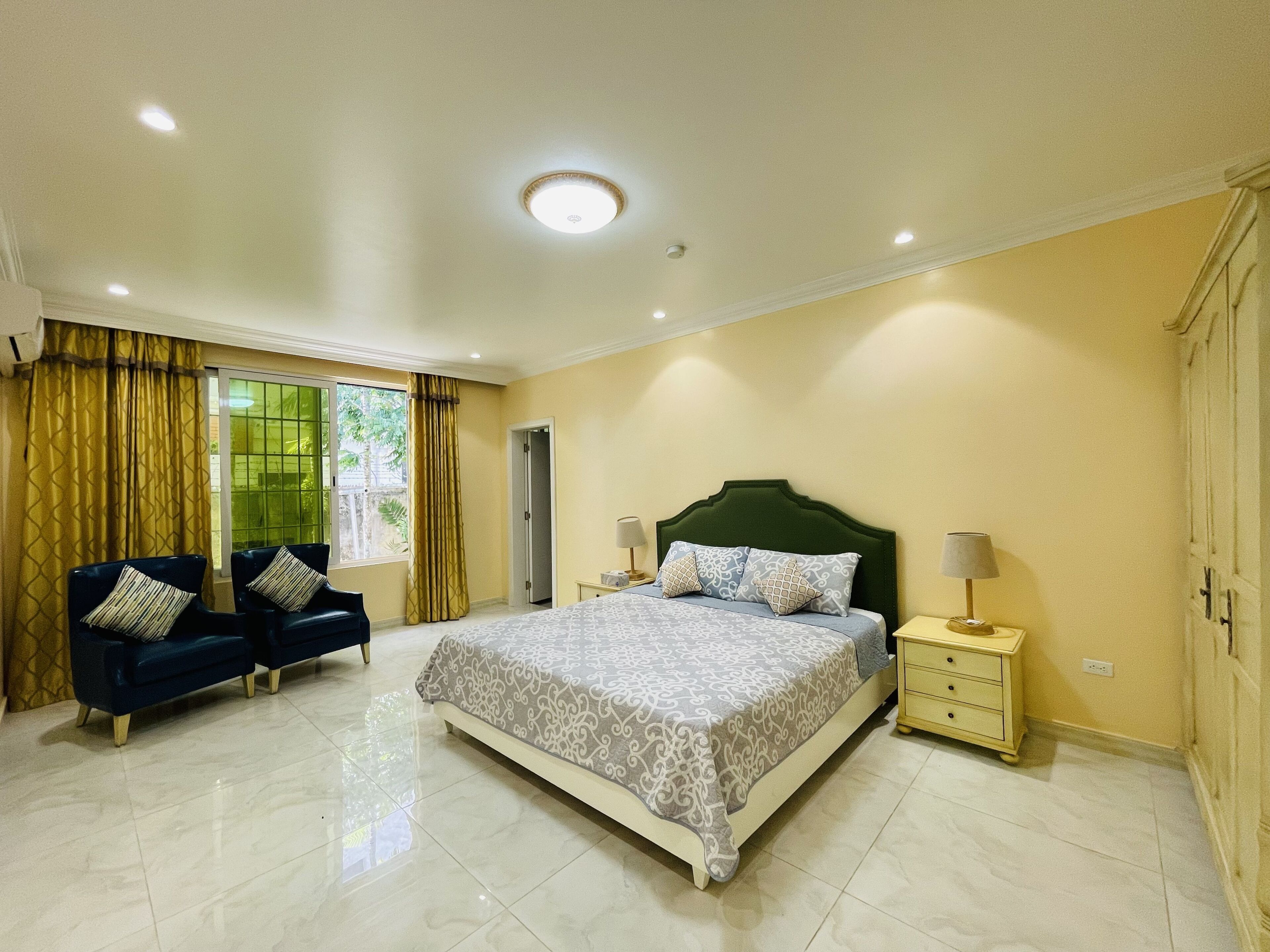 A bedroom with a large bed, two bedside tables, a nightstand, a sofa, and a window with curtains.