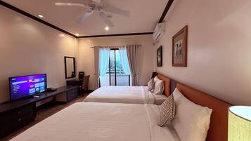 A hotel room with two beds, a TV, a ceiling fan, and a window with curtains.
