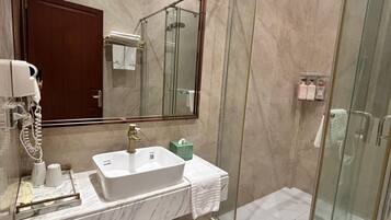 Un baño moderno con lavamanos de mármol, cabina de ducha con paredes de vidrio y un espejo grande.